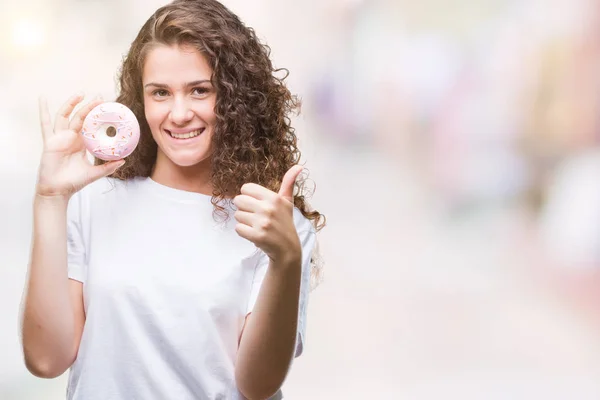 笑顔の サイン 優秀な兆候を親指をやって幸せな孤立の背景にドーナツを食べる若いブルネットの少女 — ストック写真