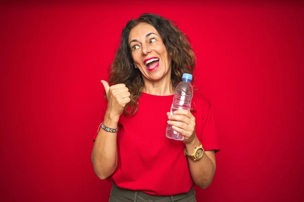 Seniorin Mittleren Alters Hält Plastikwasserflasche Über Rotem Isoliertem Hintergrund Und — Stockfoto