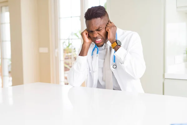 African american doctor man at the clinic covering ears with fingers with annoyed expression for the noise of loud music. Deaf concept.