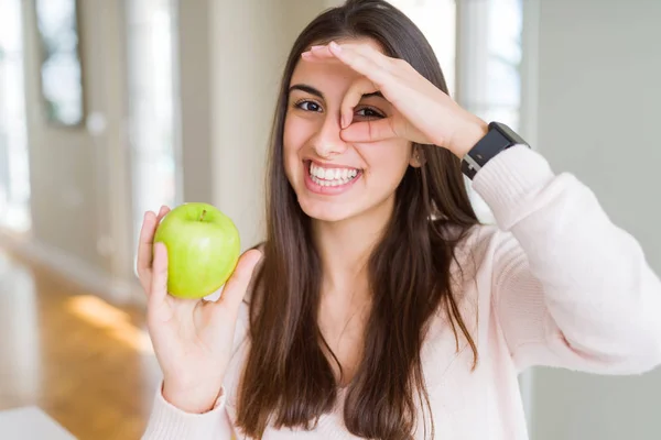 美丽的年轻女子吃健康的绿色苹果水果与快乐的脸微笑做Ok标志手对眼睛通过手指看 — 图库照片