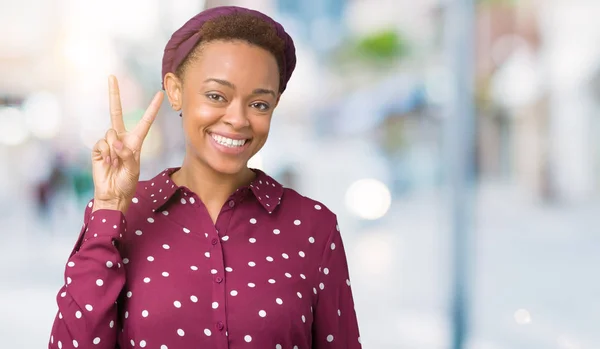 Beautiful young african american woman wearing head scarf over isolated background showing and pointing up with fingers number two while smiling confident and happy.