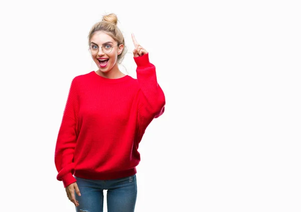 若い美しい金髪女性の分離背景人差し指の上の赤いセーターを着て メガネを成功したアイデアを着てします 終了したと満足しています ナンバーワン — ストック写真