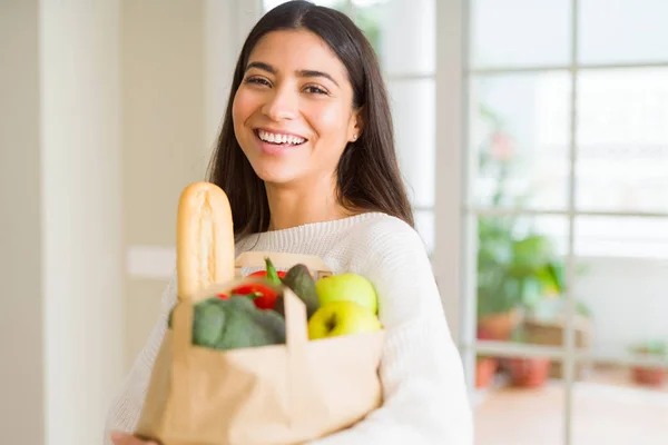 新鮮な食料品を自宅でいっぱいに紙袋を抱えた美しい若い女性 — ストック写真