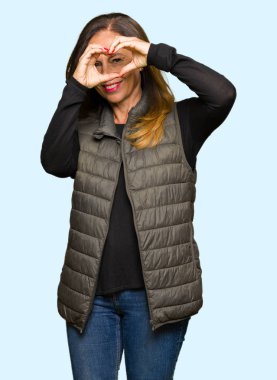 Kış yelek giyen güzel orta yaş kadın el ve parmaklar ile işaret görünümlü gülümseyen kalp şekli yapıyor