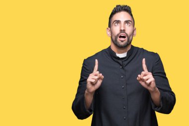 Genç Hıristiyan rahip hayrete ve yukarıya bakıyor ve parmakları ile işaret ve silah kaldırdı sürpriz izole arka plan üzerinde.