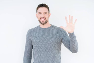 Genç yakışıklı adam izole arka plan üzerinde rahat kazak giyen gösteren ve emin ve mutlu gülümserken parmakları sayısı beş ile işaret.