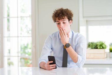 Ofiste akıllı telefonu kullanan genç iş adamı hata utancıyla şoke olan, korkunun ifadesi, sessizlikte korkma, gizli kavram ile ağız kapağı