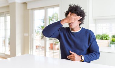 Genç afro-amerikan adam evde oturan rahat kazak giyen el ile gözleri kaplayan, ciddi ve üzgün görünümlü. Görme, gizleme ve reddetme kavramı