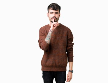 Dudaklarında parmak ile sessiz olmanı izole arka plan üzerinde kış kazak giyen genç yakışıklı adam. Sessizlik ve gizli kavramı.