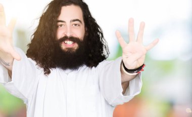 Gösterilen ve parmakları ile işaret İsa Mesih giyinen adam kendinden emin ve mutlu gülümseyerek ise dokuz numara.
