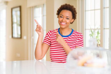 Genç güzel Afrikalı-Amerikalı kadın evde gülümseyen ve iki elleri ve parmakları ile tarafına işaret kamera bakıyor.