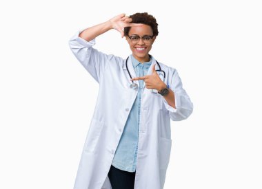 Genç Afro-Amerikan doktor kadın elle yapma çerçeve ve parmakları ile mutlu yüz gülümseyen izole arka plan üzerinde tıbbi bir palto giyiyor. Yaratıcılık ve Fotoğrafçılık kavramı.
