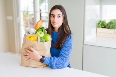 Kağıt torba sağlıklı yiyecek dolu acımak yüz ciddi düşünme emin bir ifade ile tutan güzel genç kadın
