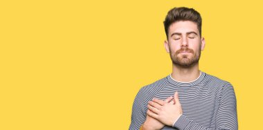 Yakışıklı delikanlı ile gülümseyen çizgili Süveter giyen kapalı gözler ve yüzünde minnettar jest ile göğüs üzerinde eller. Sağlık kavramı.