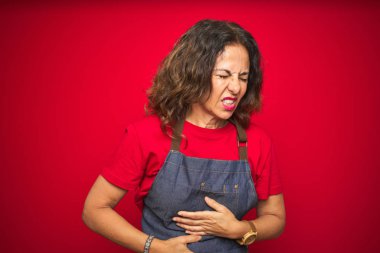 Orta yaş yaşlı kadın mide üzerinde el ile kırmızı izole arka plan üzerinde önlük üniforma giyen çünkü hazımsızlık, ağrılı hastalık kötü hissediyorum. Ağrı kavramı.