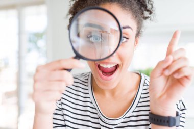 Genç Afro-Amerikalı kadın büyüteçten bakıp mutlu bir şekilde işaret ediyor.