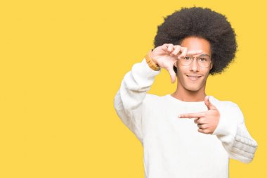 Afrikalı-Amerikalı genç afro saçlı elle yapma çerçeve ve parmakları ile mutlu yüz gülümseyen gözlüklü. Yaratıcılık ve Fotoğrafçılık kavramı.