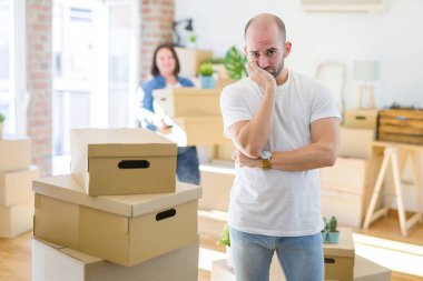 Genç çift yuvarlak karton kutular yeni bir eve hareket, kel adam evde yorgun görünümlü ve çapraz kolları ile depresyon sorunları ile sıkılmış bakarak ayakta.