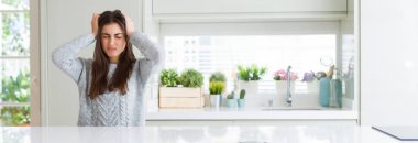 Güzel genç kadın ev umutsuz ve stresli baş ağrısı muzdarip çünkü, beyaz masada oturan geniş açı resim ağrı ve Migren. Ellerini kafasına.