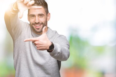 Genç yakışıklı adam elleriyle yapım çerçeve ve parmakları ile mutlu yüz gülümseyen izole arka plan üzerinde kazak giyiyor. Yaratıcılık ve Fotoğrafçılık kavramı.