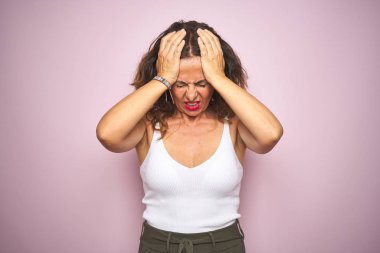 Orta yaş yaşlı kadın pembe izole arka plan üzerinde baş ağrısı umutsuz muzdarip ayakta ve stresli çünkü ağrı ve migren. Eller baş üstünde.