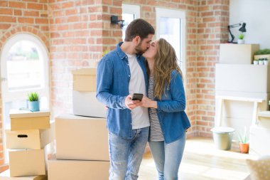 Genç çift karton kutular etrafında akıllı telefon kullanarak yeni bir eve hareket