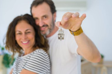Middle age senior romantic couple holding and showing house keys, hugging and smiling happy for moving to a new home clipart