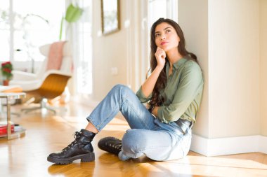 Çene düşünme hakkında soru, dalgın ifade üzerine el ile evde katta oturan genç güzel kadın. Düşünceli yüzüyle gülümsüyor. Şüphe kavramı.