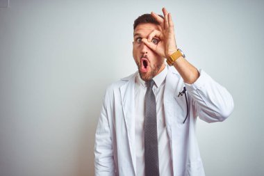 Genç yakışıklı doktor adam izole arka plan üzerinde beyaz profressional ceket giyen ok jest yaparken şaşırmış yüz ile şok, parmaklardan bakarak göz. İnanmayan ifade.