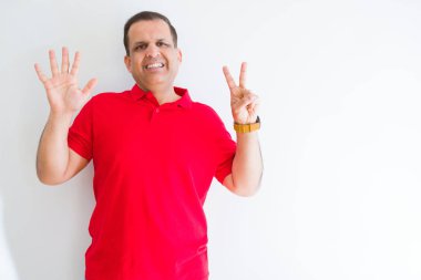 Beyaz duvar üzerinde kırmızı tişört giyen orta yaşlı adam, kendine güvenen ve mutlu gülümserken yedi numaralı parmaklarla işaret ediyor..