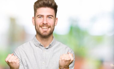 Casual gömlek kutluyor giyen genç yakışıklı adam şaşırttı ve başarı için kaldırdı Kollarını açarak hayret ve gözleri açık. Kazanan kavramı.