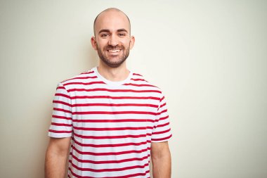 Yüzünde mutlu ve serin bir gülümseme ile beyaz izole arka plan üzerinde rahat çizgili kırmızı t-shirt giyen sakallı genç kel adam. Şanslı kişi.