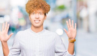 Şık gömlek gösterme ve parmakları ile işaret giyen afro saçlı Genç yakışıklı iş adamı kendinden emin ve mutlu gülümseyerek süre on numara.
