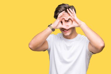 İzole arka plan yaparken kalp şekli el ve parmak işareti seyir gülümseyen ile üzerine beyaz t-shirt giyen genç yakışıklı adam