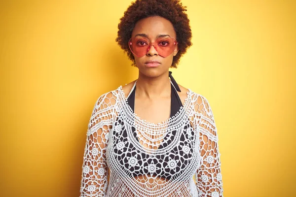 Young african american woman with afro hair wearing bikini and heart shaped sunglasses with serious expression on face. Simple and natural looking at the camera.