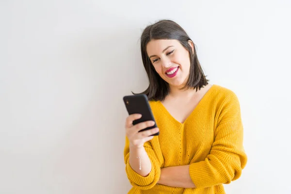美丽的黑发年轻女子微笑自信使用智能手机在孤立的白色背景穿着休闲黄色毛衣 — 图库照片