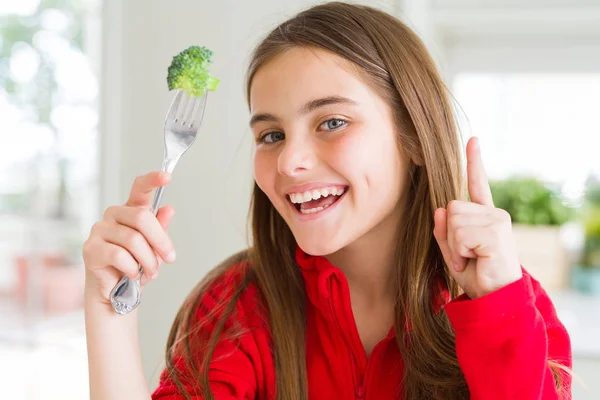 新鮮なブロッコリーを食べる美しい若い女の子は 幸せな顔で指を指すアイデアや質問に驚いた ナンバーワン — ストック写真