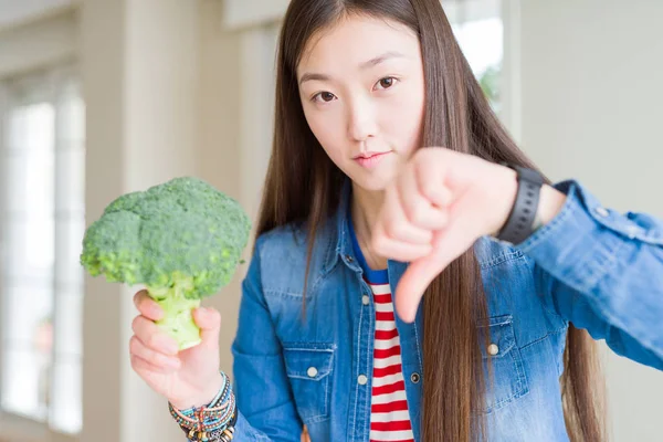 美しいアジアの女性が怒っている顔で緑の新鮮なブロッコリーを食べて 親指ダウンで嫌いを示す否定的な記号 拒絶の概念 — ストック写真