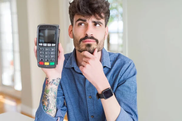 Ung Mand Med Datafon Salgssted Som Betaling Alvorligt Ansigt Tænker - Stock-foto