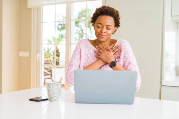 Young african american woman working using computer laptop smiling with hands on chest with closed eyes and grateful gesture on face. Health concept.