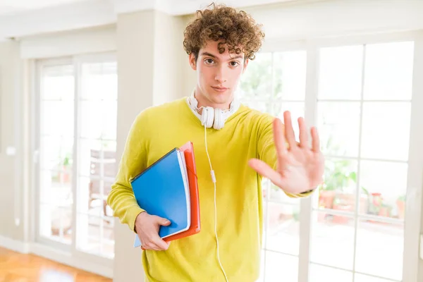 年轻的学生男子戴着耳机 拿着笔记本张开的手做停止标志与认真和自信的表情 防御手势 — 图库照片