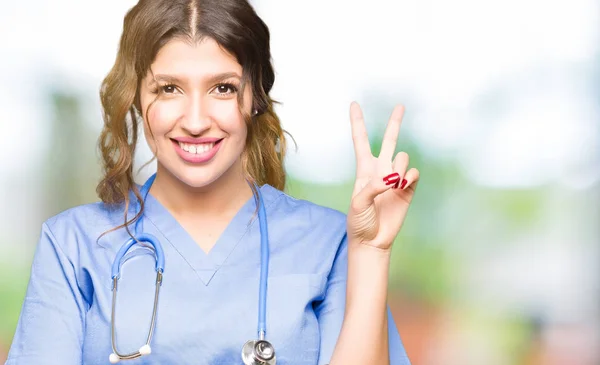 年轻的成年医生妇女穿着医疗制服微笑着 幸福的脸对着镜头眨眼做胜利的标志 — 图库照片