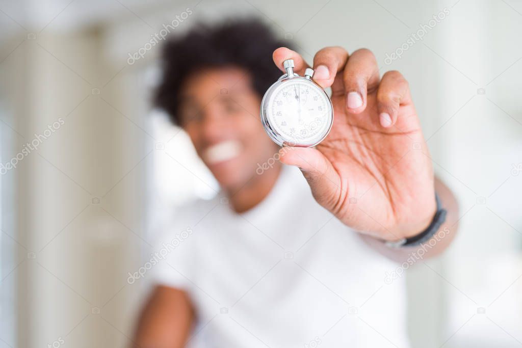 African American man holding stopwatch with a happy face standing and smiling with a confident smile showing teeth