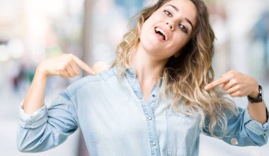 Yüzünde gülümseme ile kendinden emin görünüyorsun, kendini gururlu ve mutlu parmakları ile işaret izole arka plan üzerinde sarışın güzel genç kadın.