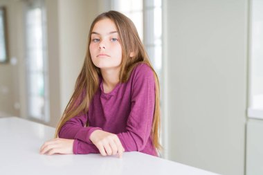 Yüzünde ciddi bir ifade ile beyaz masada güzel genç kız çocuk. Kameraya basit ve doğal bir bakış.