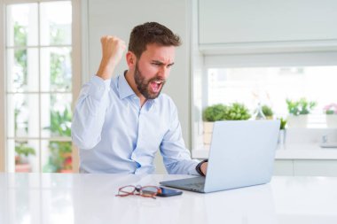 Yakışıklı iş adamı bilgisayar dizüstü kullanarak çalışan sinirli ve sinirli öfke ile bağırarak, deli ve yükseltilmiş el ile bağırıyor, öfke kavramı