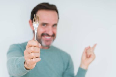 Üst düzey adam izole arka plan üzerinde gümüş çatal tutan çok mutlu yan el ve parmak ile işaret