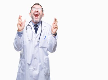 Orta yaş üst düzey ağarmış doktor umut ve gözleri kapalı geçiş parmaklarıyla gülümseyen Tıbbi üniforma izole arka plan giyen adam. Şans ve batıl kavramı.