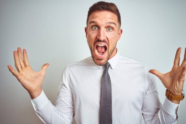 Genç yakışıklı iş adamı izole arka plan üzerinde zarif beyaz gömlek giyen deli kutluyor ve kollarını kaldırdı ve açık gözleri heyecan çığlık ile başarı için hayran. Kazanan kavramı