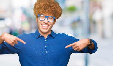 Yüzünde gülümseme ile kendinden emin görünüyorsun, kendini gururlu ve mutlu parmakları ile işaret mavi gözlük takan afro saçlı Genç yakışıklı adam.